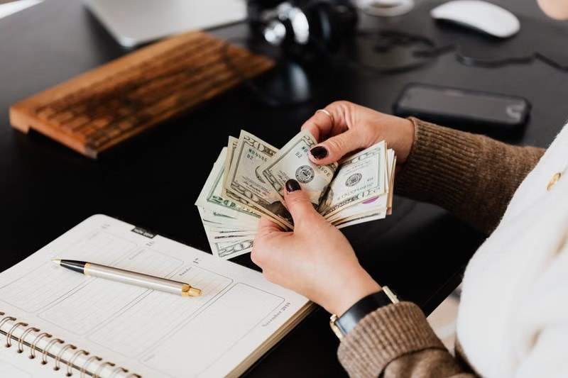 Woman counting US dollar bills beside an open planner